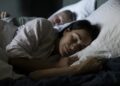 Woman sleeping on bed beside man in bedroom at home
