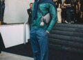Imagen que muestra a Stormzy de pie, vestido con ropa elegante, sosteniendo una bolsa y con accesorios, en un evento de moda.